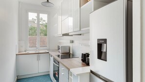 Een kleine keuken met witte kastjes, een magnetron, een waterdispenser en een koffiezetapparaat.