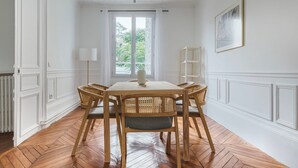 Een eetgedeelte met een houten tafel en stoelen, een vloerlamp en een raam met uitzicht op groen.
