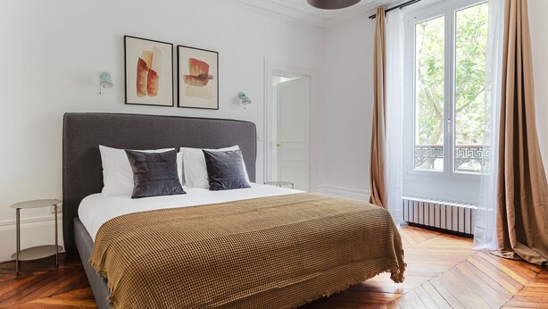 Een moderne slaapkamer met een groot bed, uitzicht op de omgeving door een raam, en een deur naar een andere kamer.