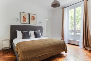 Een moderne slaapkamer met een groot bed, uitzicht op de omgeving door een raam, en een deur naar een andere kamer.