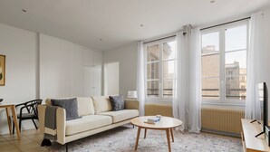 Ein modernes Wohnzimmer mit einem beigen Sofa, einem runden Couchtisch und einem großen Fenster mit Vorhängen.