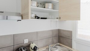A modern kitchen with white cabinets, grey tiles, a stainless steel sink, and a toaster. - Blueground | Jardin du Luxembourg, walk to gardens (Paris)