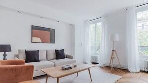 A modern living room with a sofa, coffee table, and floor lamp. - Blueground | Jardin du Luxembourg, walk to gardens (Paris)
