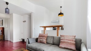 Un salon avec un canapé gris, deux coussins à motifs, une table basse en bois et une suspension.