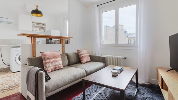 Un espace de vie compact comprenant un canapé, une table basse, un téléviseur et une fenêtre donnant sur des immeubles.