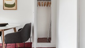 Une pièce comprenant une table ronde, une chaise grise, une œuvre d’art encadrée et un portant à vêtements avec des cintres.
