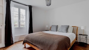 Ein Schlafzimmer mit einem Bett, zwei Nachttischen, einer Hängeleuchte und einem Fenster mit Vorhängen.