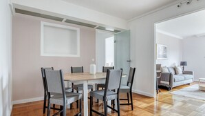 Un comedor moderno con una mesa de madera y sillas grises tapizadas, un espejo grande en la pared, y un sofá gris en la sala de estar contigua.