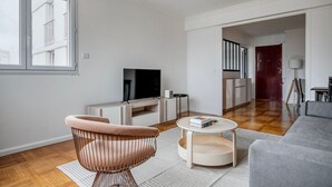 Una sala de estar moderna con televisor, una butaca rosa, un sofá gris y una mesa de centro redonda.