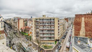 Un edificio de varios pisos con balcones, una calle en primer plano y otros edificios al fondo.