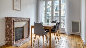 A dining area with a marble fireplace, a table with chairs, and a view of buildings through large windows. - Blueground | Champ de Mars, walk to Eiffel Tower (Paris)