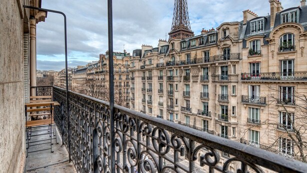 A balcony with wrought iron railings overlooking a row of historic buildings and the Eiffel Tower in the background. - Blueground | Champ de Mars, walk to Eiffel Tower (Paris)
