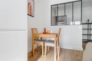 Un espace repas moderne avec une table et des chaises en bois, un tableau encadré au mur et une grande fenêtre donnant sur la cuisine.