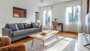 A modern living room with a grey sofa, a wooden coffee table, and a small desk with a chair. - Blueground | Quartier Latin, near gardens (Paris)