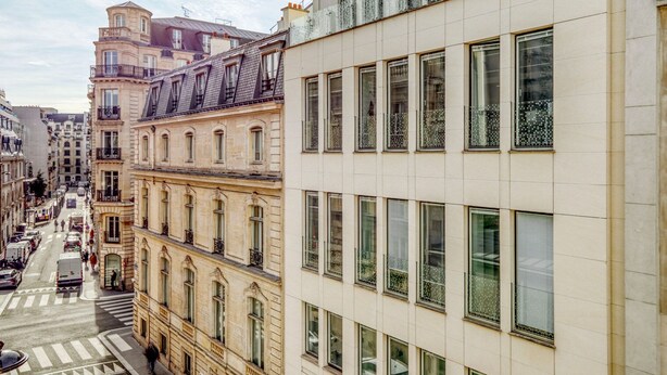 Vista de una calle en una ciudad con edificios históricos, un paso de peatones y cielo despejado.
