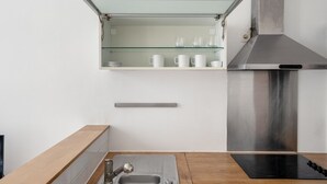 Una cocina moderna con una campana de acero inoxidable, un estante de vidrio con tazas blancas y una encimera de madera.
