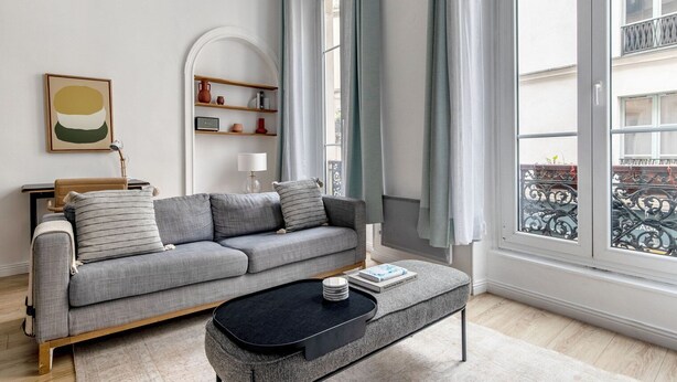 Una sala moderna con un sofá gris, una mesa de centro negra y una estantería.