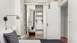 Un dormitorio con cama, lámpara de noche y un vestidor con estantes y espacio para colgar ropa.