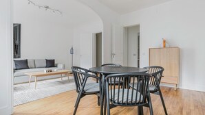 A modern living room with a round dining table, grey sofa, and wooden flooring.