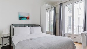 A modern bedroom with a bed, a bedside table, a lamp, a painting, and a view through a large window.