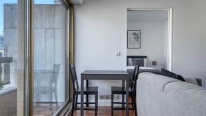 Une pièce moderne comprenant une table à manger et des chaises, un canapé gris et une grande fenêtre donnant sur la ville.