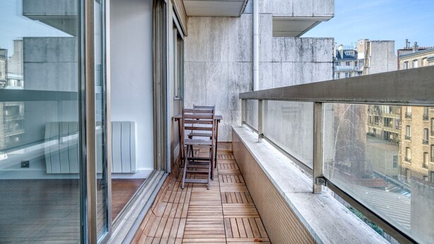 Un balcon doté d’un plancher en bois, d’une rambarde en métal et offrant une vue sur le paysage urbain.