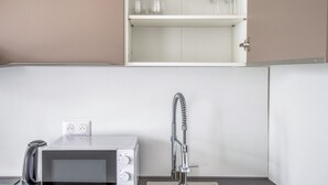 A kitchen with a microwave, a faucet, and a cabinet with wine glasses.