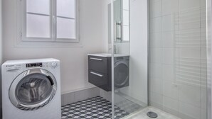 A compact bathroom with a washing machine, a small cabinet, and a glass shower enclosure.
