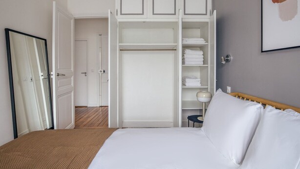 A bedroom with a bed, a wardrobe, and a door leading to another room.