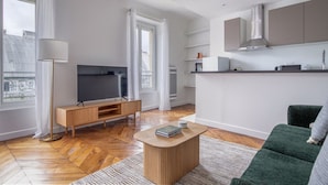 A modern living room with a flat-screen TV, wooden entertainment unit, and a green sofa.