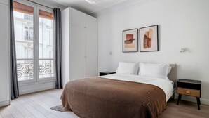 A bedroom with a bed, nightstands, a window with curtains, and two abstract paintings on the wall. - Blueground | Pigalle, nr restaurants & boutiques (Paris)