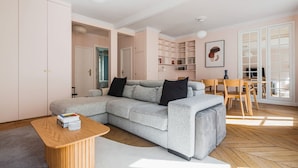 A modern living room with a grey sectional sofa, wooden coffee table, and a dining area with a wooden table and chairs. - Blueground | Pigalle, nr dining & shopping (Paris)