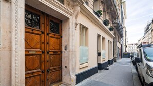 A narrow street with a row of buildings featuring large wooden doors and windows. - Blueground | Pigalle, nr dining & shopping (Paris)