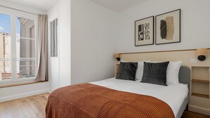 A bedroom with a bed, a window with curtains, and two wall-mounted artworks. - Blueground | Jardin des Plantes, nr Notre Dame (Paris)