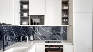 A modern kitchen with a black marble backsplash, white cabinetry, and a built-in oven. - Blueground | Batignolles, near park & restaurants (Paris)