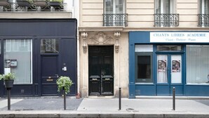 A building facade with a black door, a blue entrance, and a sign reading "CHANTS LIBRES ACADEMIE" indicating a venue for chant, theatre, and piano. - Blueground | Batignolles, near park & restaurants (Paris)