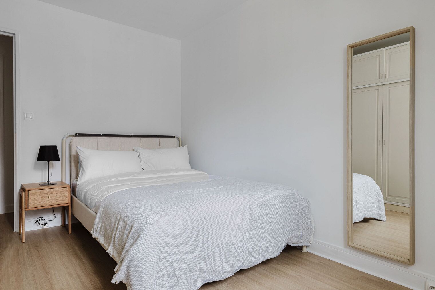 A bedroom with a bed, a nightstand, a mirror, and a wardrobe.