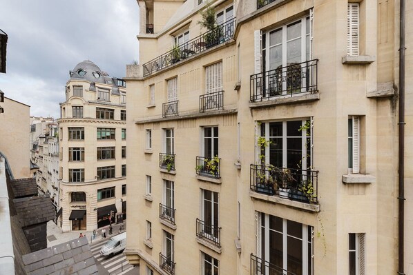 A multi-story building with balconies, windows with shutters, and a street view.