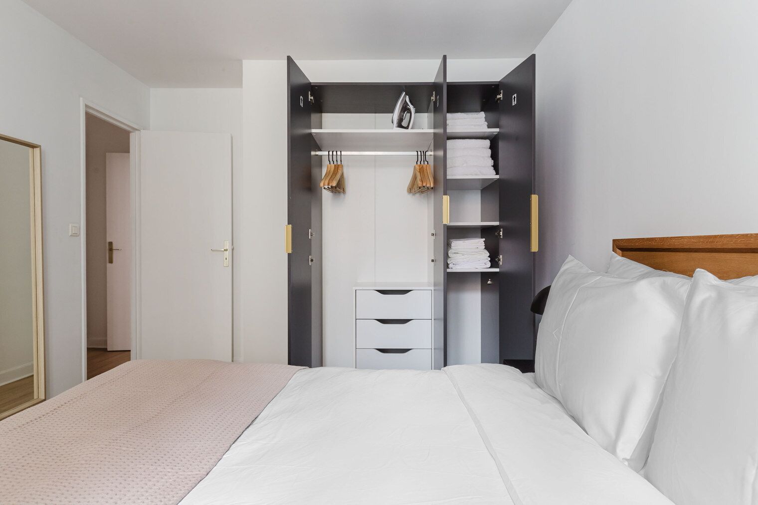 A bedroom with a bed, a wardrobe with hanging space, and a door leading to another room.