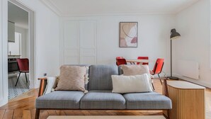 A modern living room with a grey sofa, red chairs, a wooden coffee table, and a floor lamp. - Blueground | Batignolles, near park & dining (Paris)