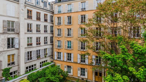 A multi-story building with uniform window shutters and balconies, surrounded by lush greenery. - Blueground | Batignolles, near park & dining (Paris)