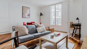 A modern living room with a grey sofa, a wooden coffee table, and a red dining table. - Blueground | Batignolles, near park & dining (Paris)