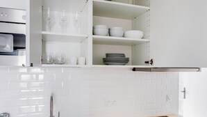 A modern kitchen with white cabinetry, a built-in oven, and a black induction cooktop. - Blueground | Batignolles, near park & dining (Paris)