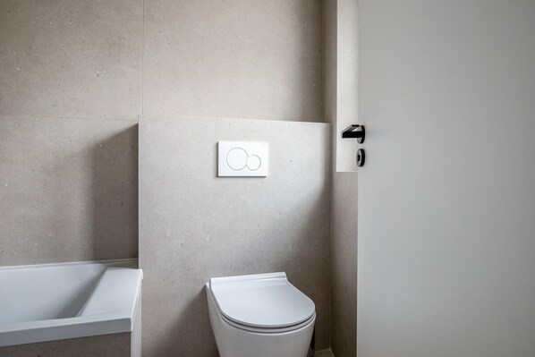 A modern bathroom with a toilet, a wall-mounted flush handle, and a bathtub.