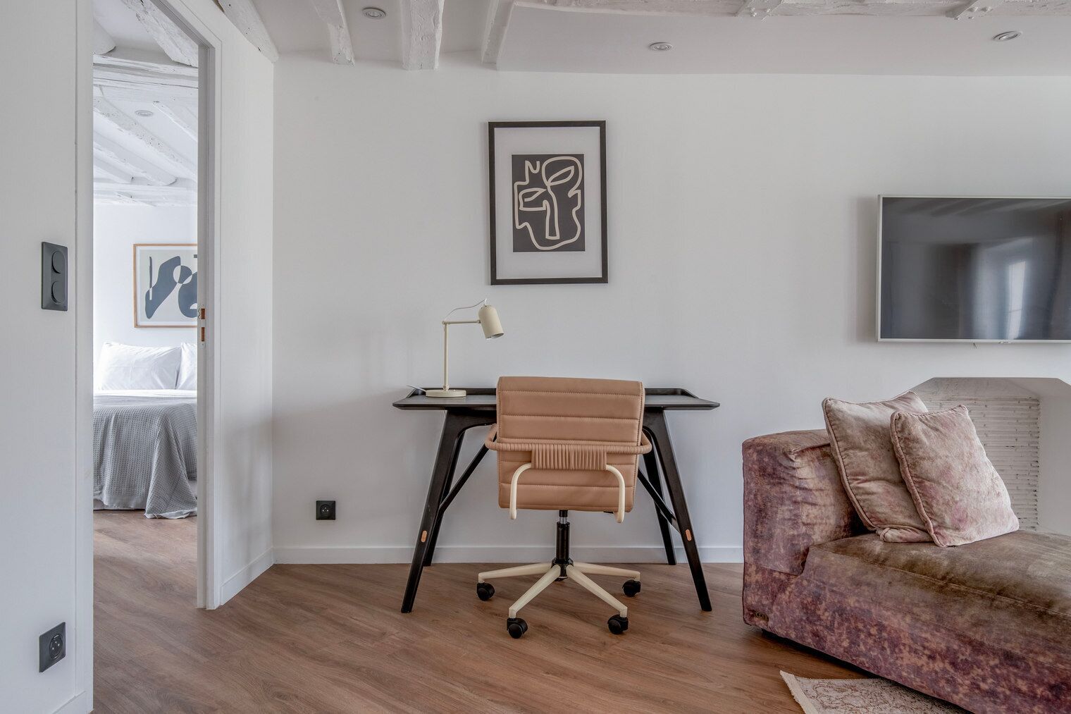 Un salon moderne avec un bureau, un fauteuil marron, un canapé rose et une œuvre d’art abstraite encadr ée accrochée au mur.