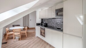 Une cuisine moderne avec des meubles blancs, un plan de travail noir et un four encastré. On y trouve également un coin repas avec une table ronde et des chaises en bois.
