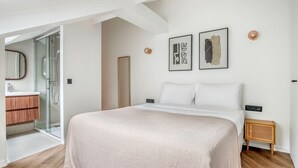 Une chambre moderne avec un grand lit, une table de chevet en bois, une commode, un miroir et un espace douche.