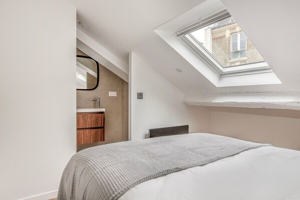 Une chambre à coucher avec un puits de lumière, un lit, une table de chevet et une armoire en bois.