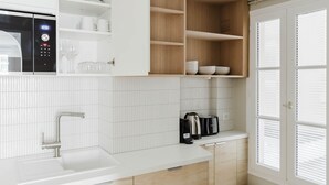 A modern kitchen with white cabinetry, a built-in microwave, a sink, and a coffee maker.