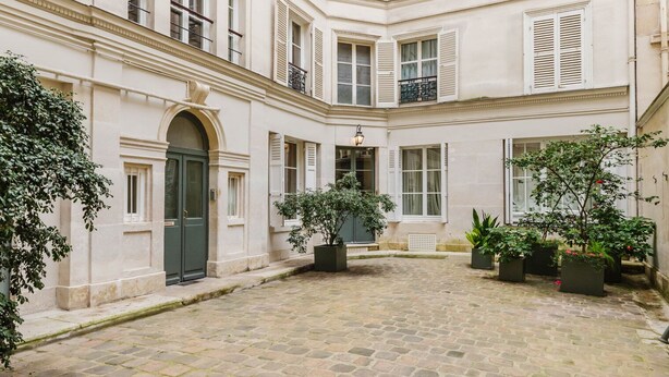 A courtyard with a cobblestone floor, a central fountain, and potted plants.